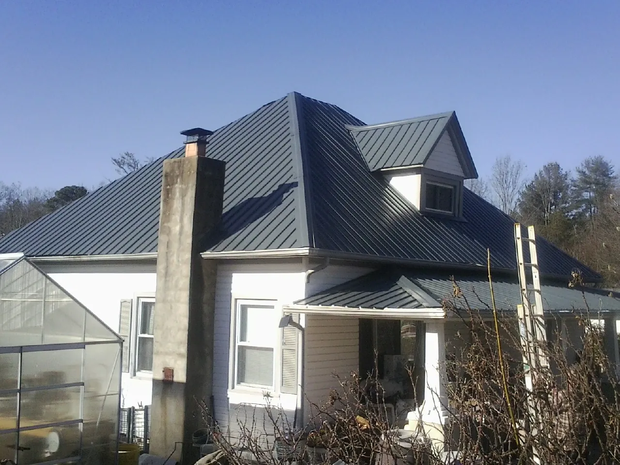 Dark blue standing seam metal roof on a white farmhouse with dormer — Slate & Tile Roof Repair by Roofing Brothers in Ringling