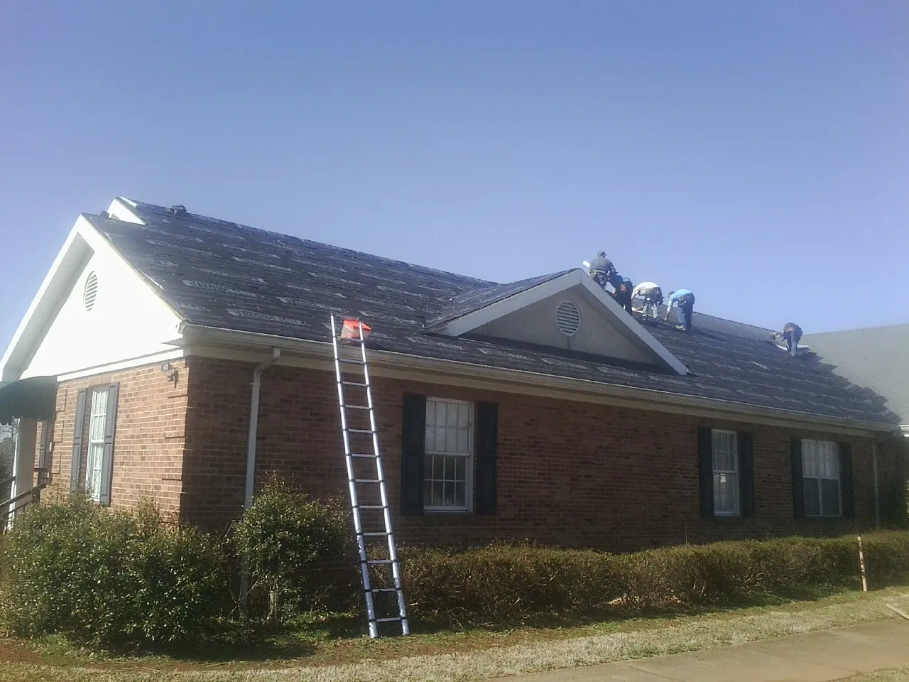 Crew tearing shingles off a brick ranch roof with a ladder set — Metal Roof Repair work by our crew in Ringling
