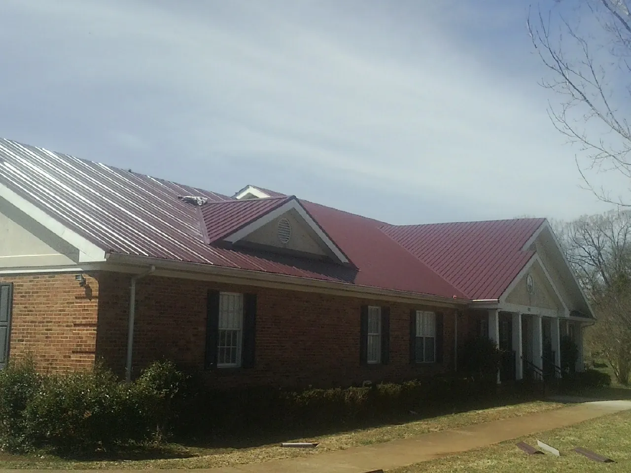 Red metal roof with gabled entries on a long brick building, from a Hail Damage Roof Repair job in Ringling