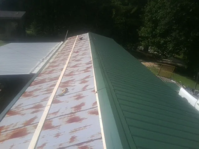 Old rusted panels beside newly installed green metal roofing — Wind Damage Roof Repair by Roofing Brothers in Ringling