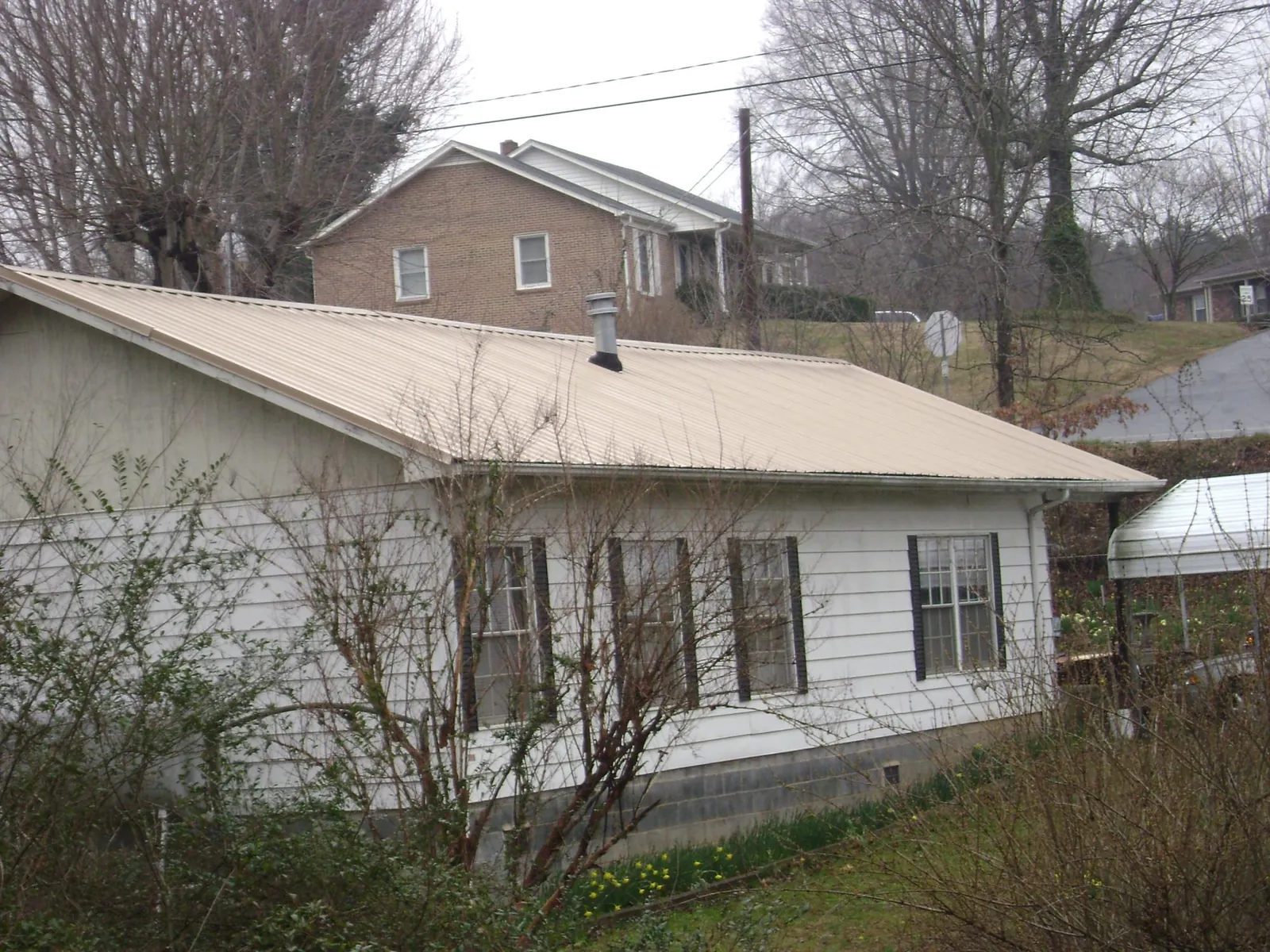 Tan metal roof on a white sided house set into a hillside — Commercial Roofing by Roofing Brothers in Ringling